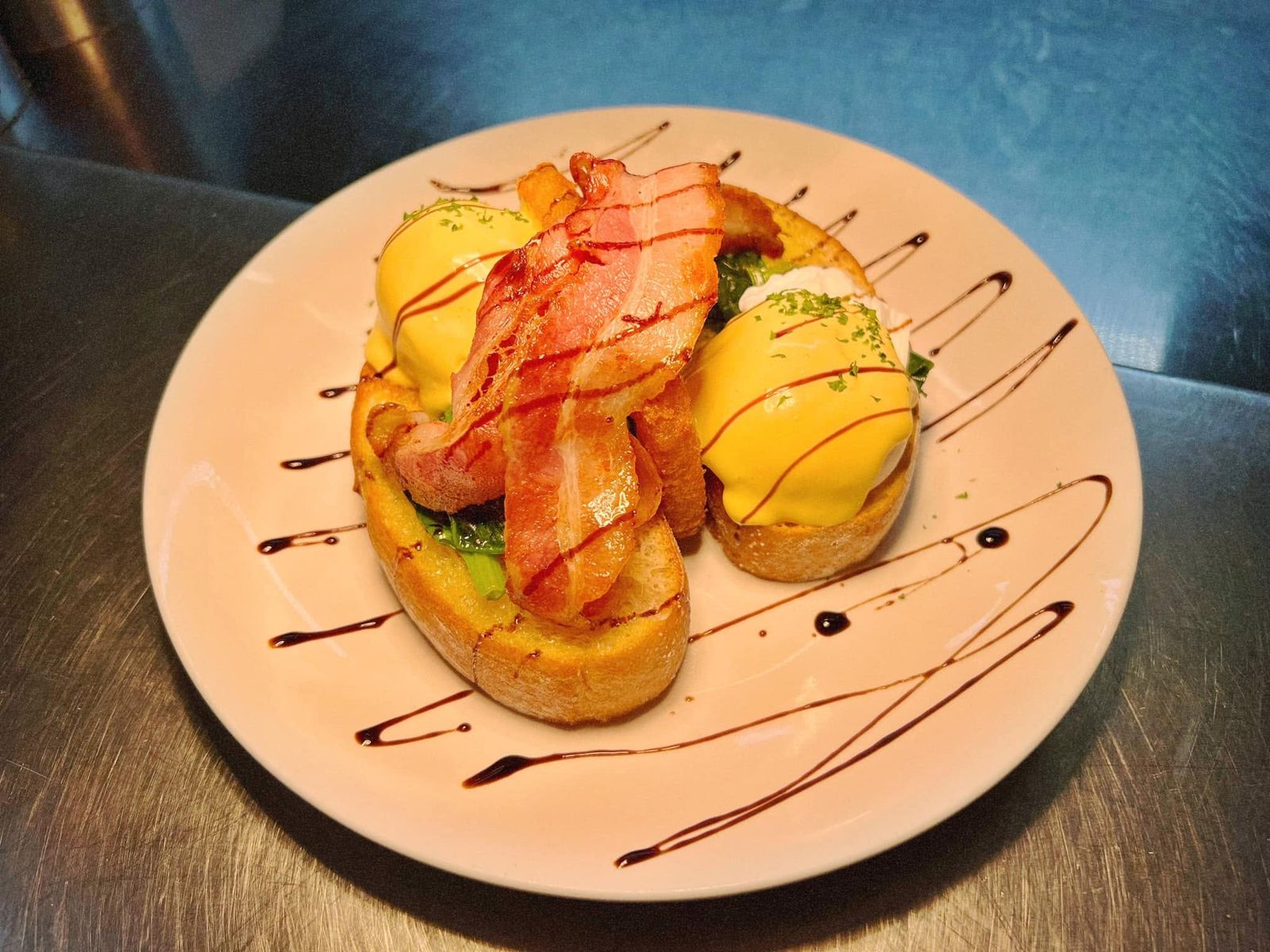 Huevos pochados con salsa holandesa, panceta crocante y espinaca sobre pan tostado, con reducción de aceto